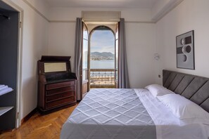 Una camera da letto con un letto, una cassettiera, uno specchio e vista su un corpo d'acqua attraverso una finestra ad arco.