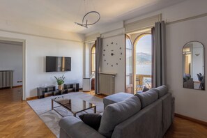 Un soggiorno moderno con divano, televisione e vista sul mare attraverso ampie finestre.