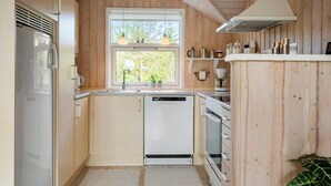 Een compacte keuken met houten wanden, een raam met uitzicht, een vaatwasser en een fornuis.