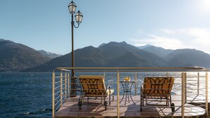 Eine Terrasse mit zwei Stühlen und einem Tisch, mit Blick auf ein Gewässer und Berge.