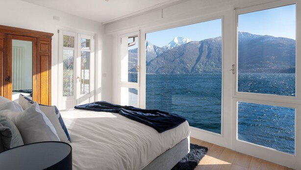 Ein Schlafzimmer mit großem Fenster, einem Bett und Blick auf einen Berg und Wasser.