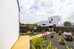 A modern outdoor patio with a stone wall, a small wooden structure, and various plants. - Villa Lajares Dos - Two Bedroom Villa, Sleeps 4 (Lajares)