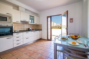 A modern kitchen with white cabinets, a black countertop, and a dining area with a glass table and chairs. - Villa Lajares Dos - Two Bedroom Villa, Sleeps 4 (Lajares)