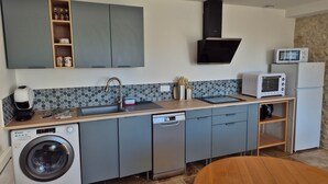 A compact kitchen with grey cabinets, a built-in washing machine, a dishwasher, a microwave, and a coffee machine. - La P'tite Pierre (Ineuil)