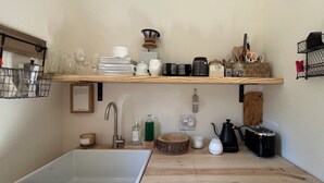 Ett kök med en vit diskho, trähyllor, en kaffebryggare och diverse köksredskap.