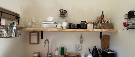 Eine Küche mit einem weißen Spülbecken, Holzregalen, einer Kaffeemaschine und verschiedenen Küchenutensilien.