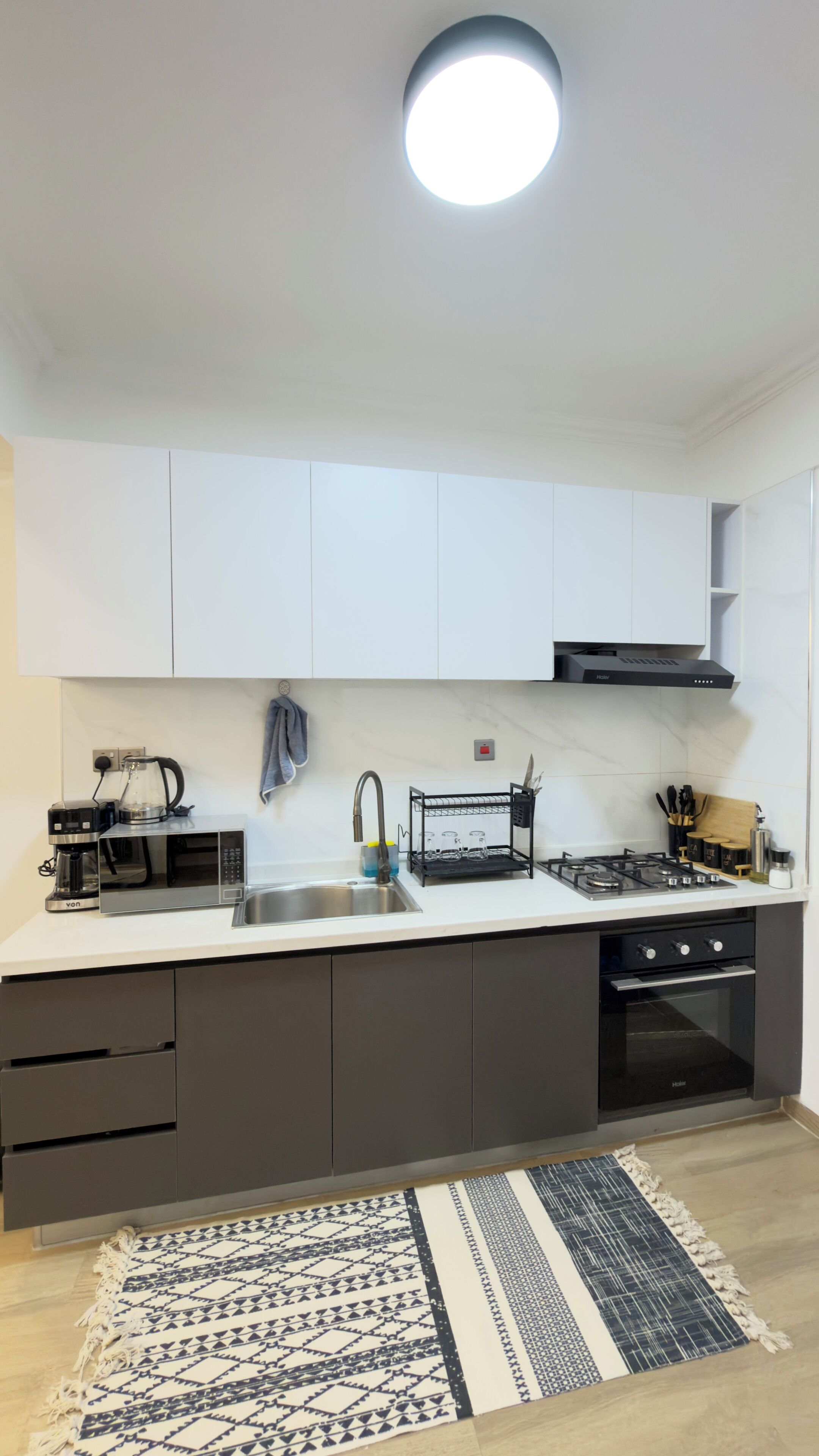 Una cocina moderna con armarios blancos, un lavamanos de acero inoxidable, una estufa a gas y una cafetera.
