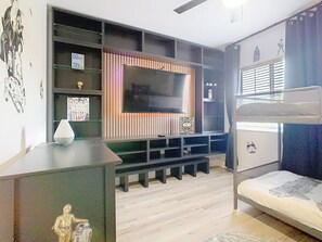 Ein Zimmer mit einem Etagenbett, einem an der Wand befestigten Fernseher, einem Schreibtisch mit Lampe und Star Wars-Dekorationen.