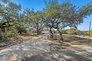 A residential area with a gravel driveway, trees, and a house with a garage. - Crossbow Canyon Retreat w/Hot tub! (Canyon Lake)