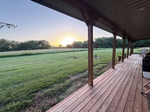 Una terraza de madera con vistas a un campo cubierto de hierba y un atardecer.