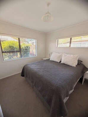 A bedroom with a large bed, two bedside tables, and a ceiling light. - Hosts on the Coast Crown Reef Cottage (Pauanui)