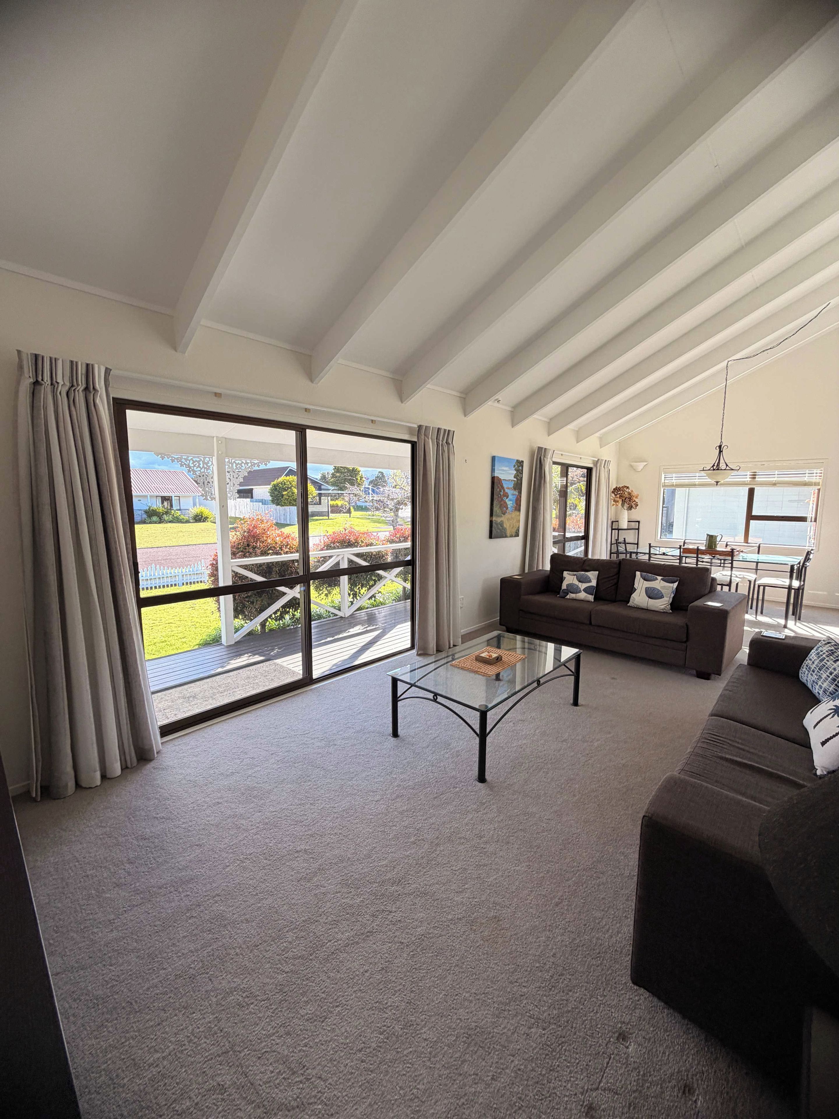 A spacious living room with a large sliding glass door leading to a deck, a glass coffee table, and a sofa.