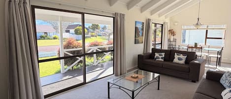 A spacious living room with a large sliding glass door leading to a deck, a glass coffee table, and a sofa.