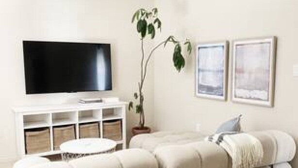A living room with a sectional sofa, a flat-screen TV, a small round coffee table, and two framed pictures on the wall. - Chic 2BR Mount Pleasant Suite Near Downtown (Vancouver)