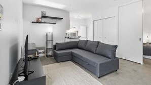 A modern living room with a grey sectional sofa, a flat-screen TV, a floor lamp, and a white door. - Bright Private-Entrance Suite, Quiet East Van (Vancouver)