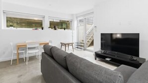 A modern living room with a sofa, TV, dining table, chairs, and a staircase leading to an upper level. - Bright Private-Entrance Suite, Quiet East Van (Vancouver)
