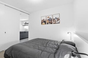 Quarto moderno com uma cama grande, uma mesa de cabeceira e uma luminária fixada na parede.