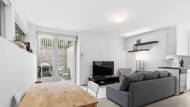A modern living room with a sofa, a TV, a wooden table, and a kitchen area with a fridge and cabinets. - Bright Private-Entrance Suite, Quiet East Van (Vancouver)