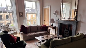 A living room with a sofa, armchair, coffee table, fireplace, and large windows. - Luxurious apartment in the New Town. Walking distance from central Edinburgh (Edinburgh)