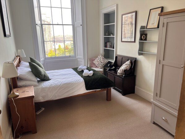 Un dormitorio con cama, lámparas de noche, cómoda, armario y ventana con vistas.