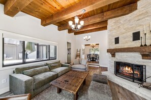 Ein Wohnzimmer mit Kamin, Holzbalkendecke, einem großen Fenster und einer Couch.