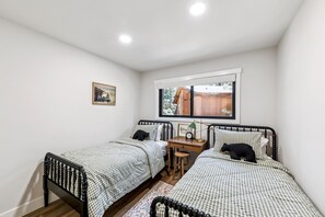 Ein Schlafzimmer mit zwei Betten, einem Schreibtisch, einem Fenster und einem Bild an der Wand.