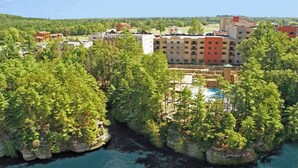 Ett semesterområde med en stor byggnad, en swimmingpool och en naturskön omgivning med träd och vatten.