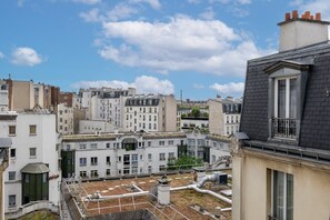 Eine Dachterrasse mit Blick auf eine Stadtlandschaft, darunter mehrstöckige Gebäude und ein klarer Himmel.