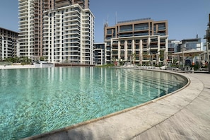 Ein Pool mit gewölbter Kante, umgeben von einer Betonplattform. Im Hintergrund sind mehrstöckige Wohngebäude mit Balkonen zu sehen.