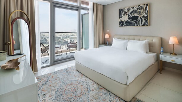 A hotel room with a large bed, a view of the city, a balcony with a chair, and a painting on the wall. - Chic 2BR in Paramount Midtown Infinity Pool Access (Dubai)