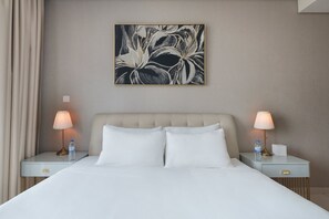 Ein Hotelzimmer mit einem Bett, zwei Nachttischen, Lampen, einer Wasserflasche und einem gerahmten Kunstwerk an der Wand.