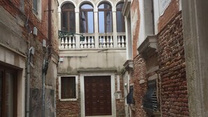 A narrow alleyway with a central door, flanked by buildings with brick facades and a balcony with white balustrades. - Stradivari apartment in Venice historic center (Venezia)