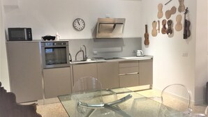A modern kitchen with a microwave, oven, and stainless steel appliances. There is a glass dining table with chairs and a clock on the wall. - Stradivari apartment in Venice historic center (Venezia)