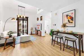 Een moderne woonkamer met een bank, een salontafel, een eethoek met een tafel en barstoelen, een televisie en een ingelijste foto aan de muur.
