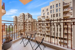 Een balkon met een tafel, stoelen, een bloempot en uitzicht op omliggende gebouwen.