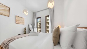A bedroom with a bed, pillows, a bedside table, a chair, a hanging light fixture, and a window with curtains. - Free Housekeeping Visits During Your Stay - Stayshort - Cozy Townsquare 1 Bed Apartment With Balcony That Sleeps 4 (Dubai)