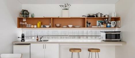 A modern kitchen with white cabinets, a microwave, and a sink. There are two stools and a wooden table.