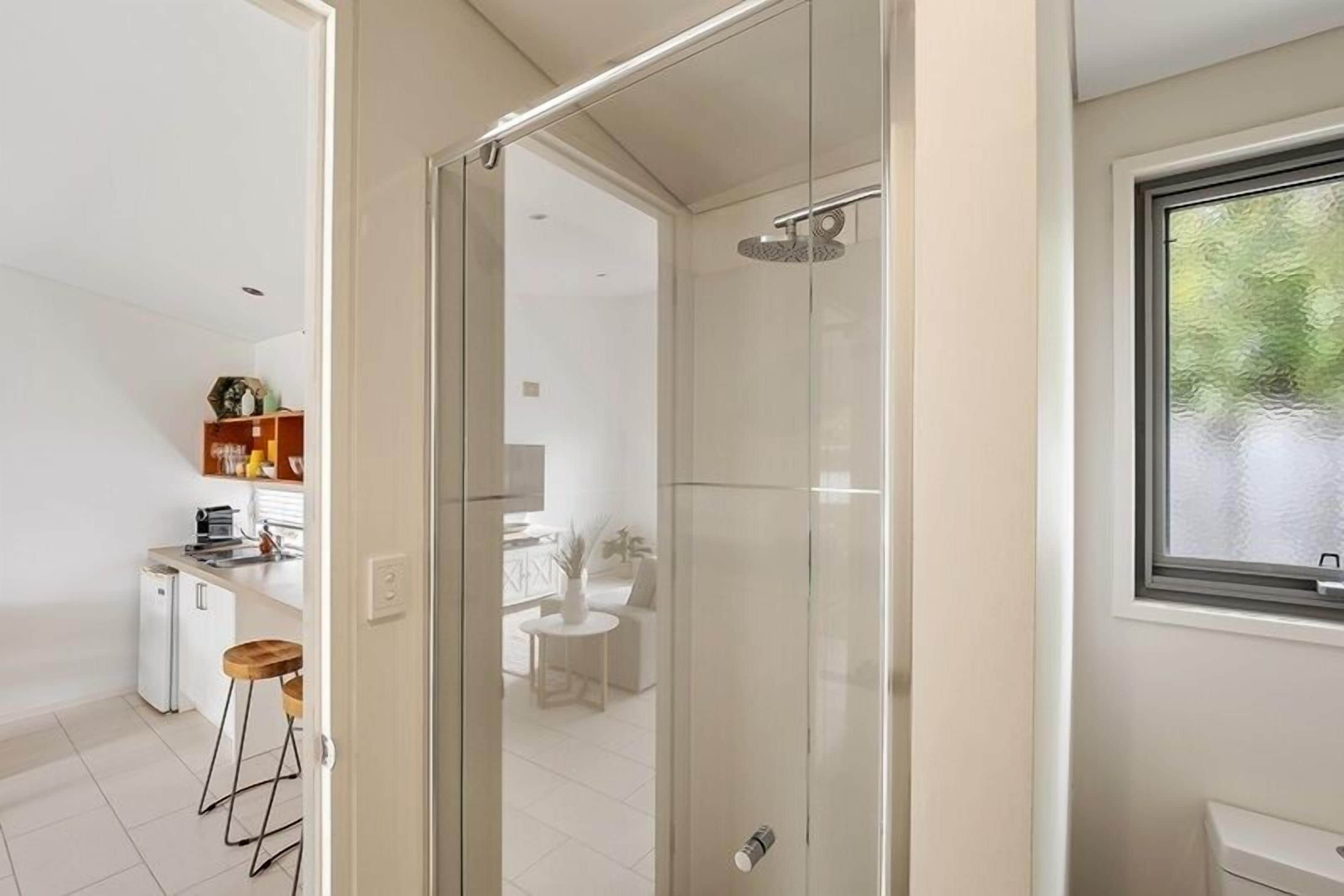 A modern kitchen with white appliances, a dining area with a white table and chairs, and a glass shower enclosure.