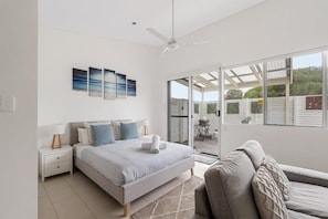 A bedroom with a bed, bedside tables, a ceiling fan, and a view through a glass door to an outdoor area.