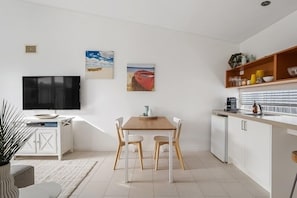 A modern kitchen with white cabinets, a wooden dining table, and a flat-screen TV.