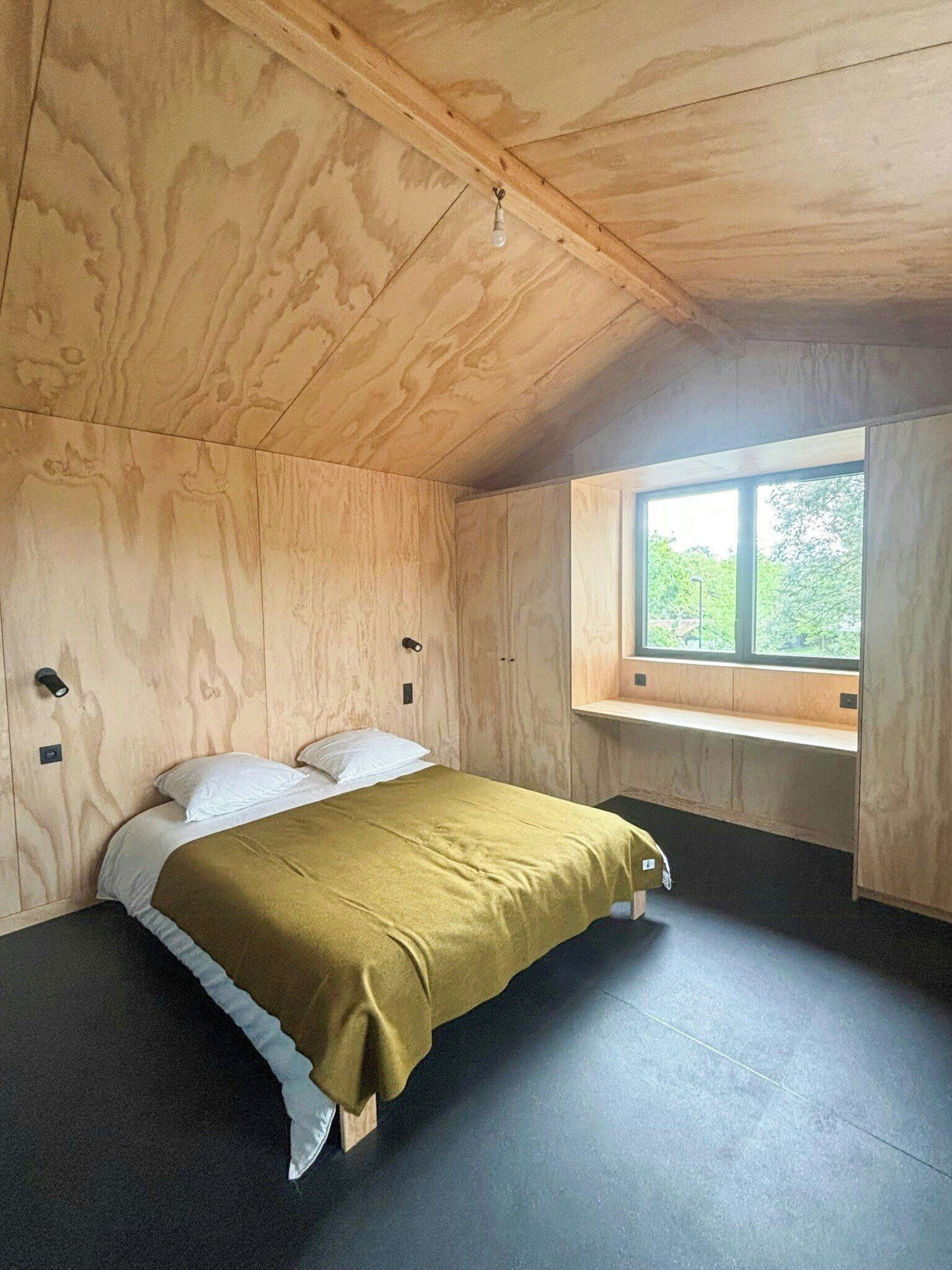 Ein Zimmer aus Holz mit einem Bett, einem Fenster und einer Sitzbank.