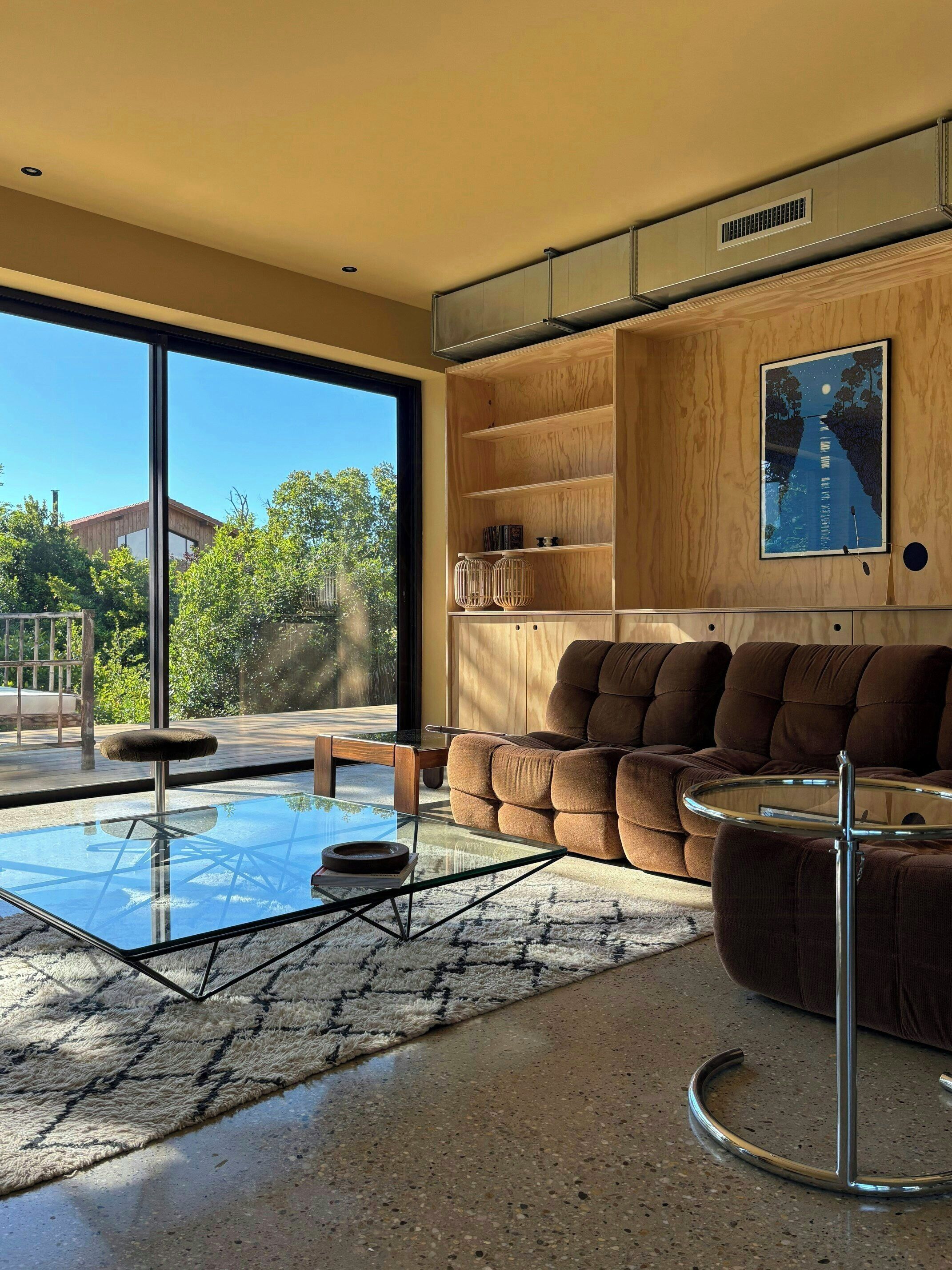 A modern living room with a glass coffee table, brown sofa, and wooden shelves.