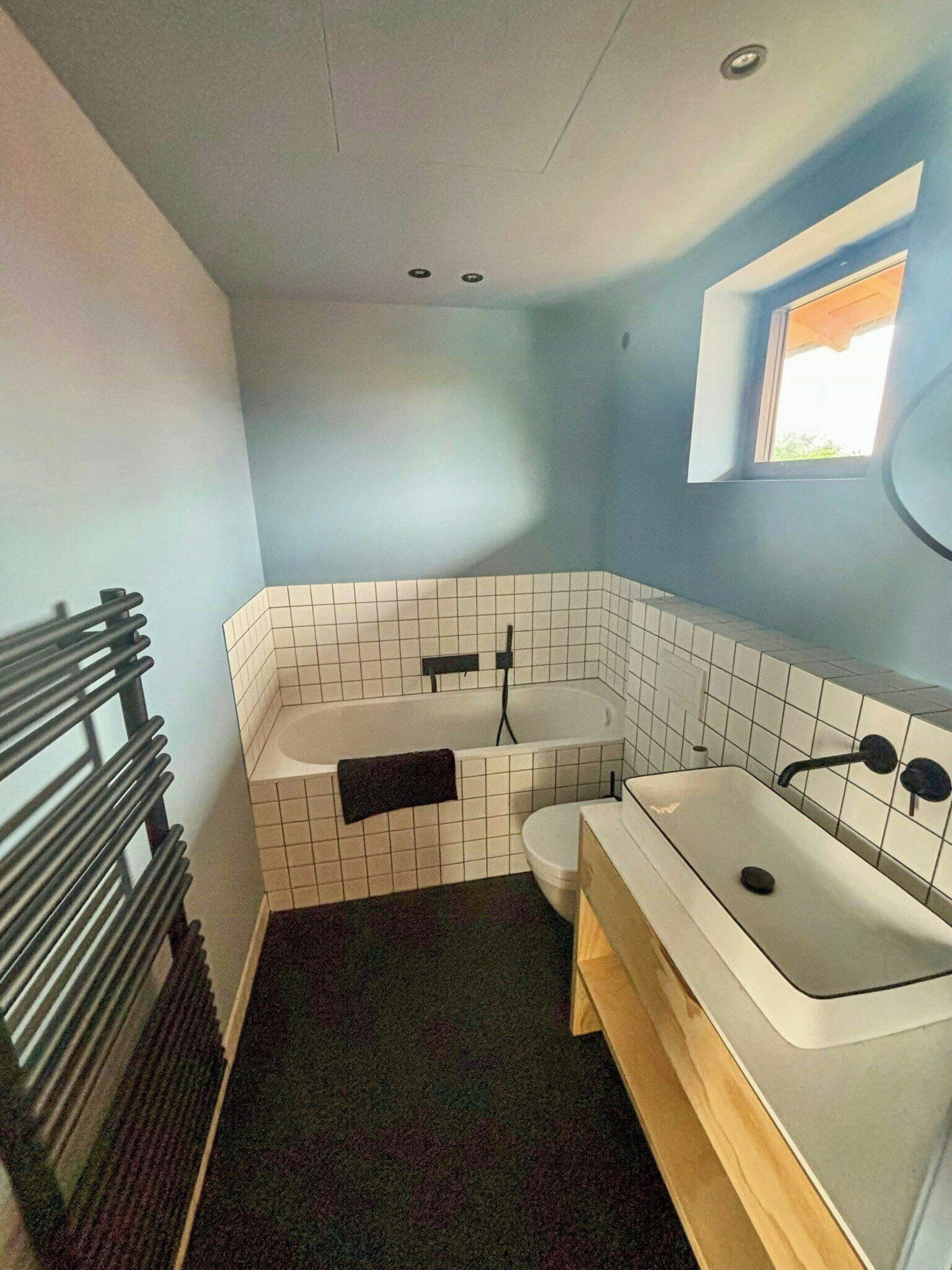 Et badeværelse med badekar, toilet og et vindue.