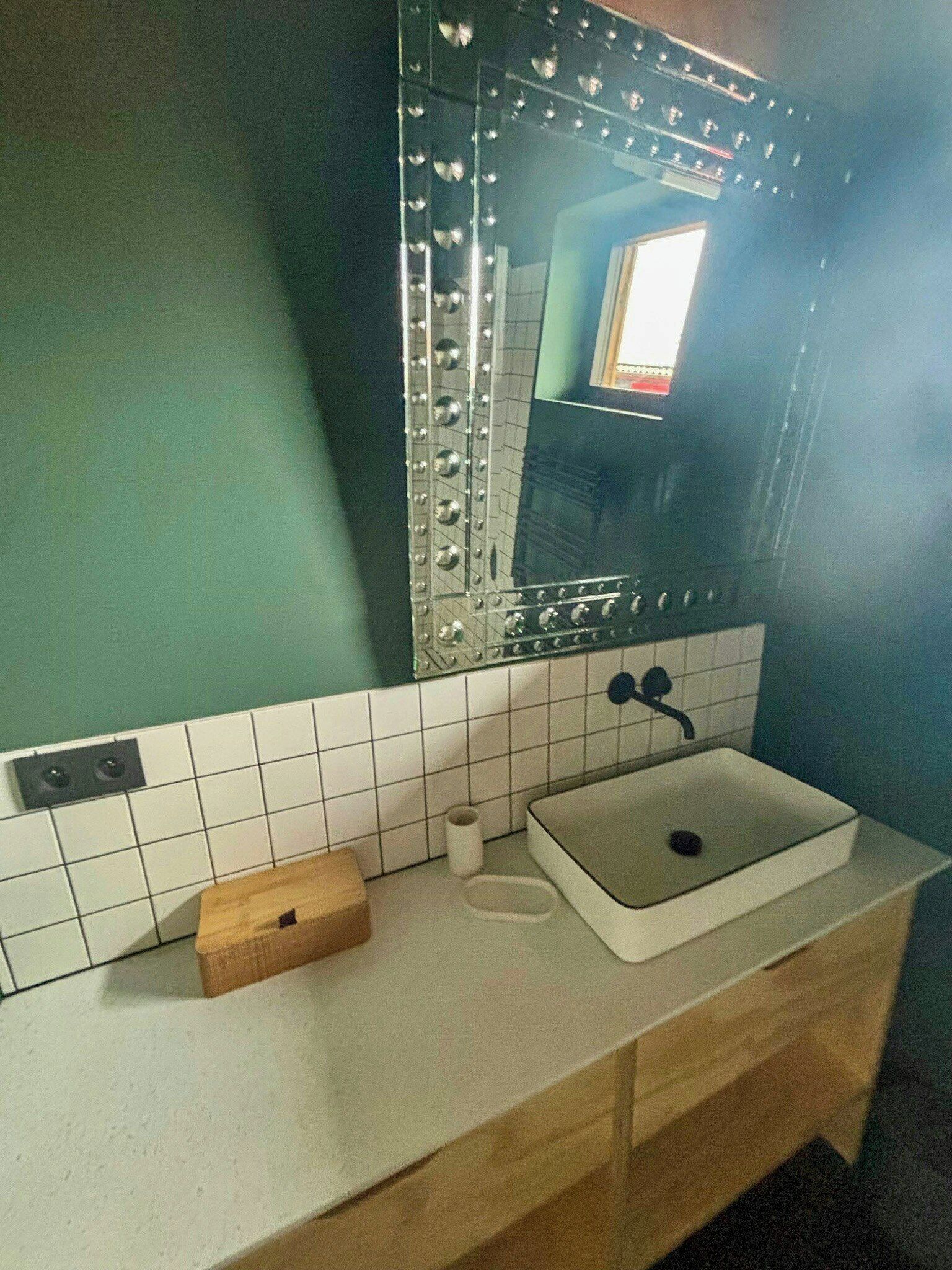 Ein Badezimmer mit einem weißen Waschbecken, einem Spiegel mit dekorativem Rahmen und einer Holzkiste auf der Ablagefläche.