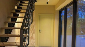 Un interior moderno con una escalera de madera, una puerta y amplios ventanales correderas.