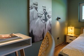 Un dormitorio con cama, mesita de noche, lámpara y un cartel en la pared.
