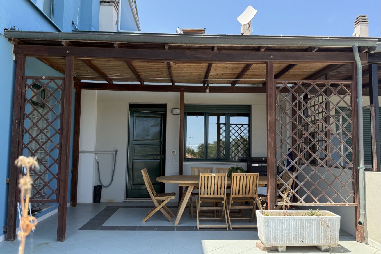Une terrasse couverte avec une table et des chaises, une porte et une fenêtre.