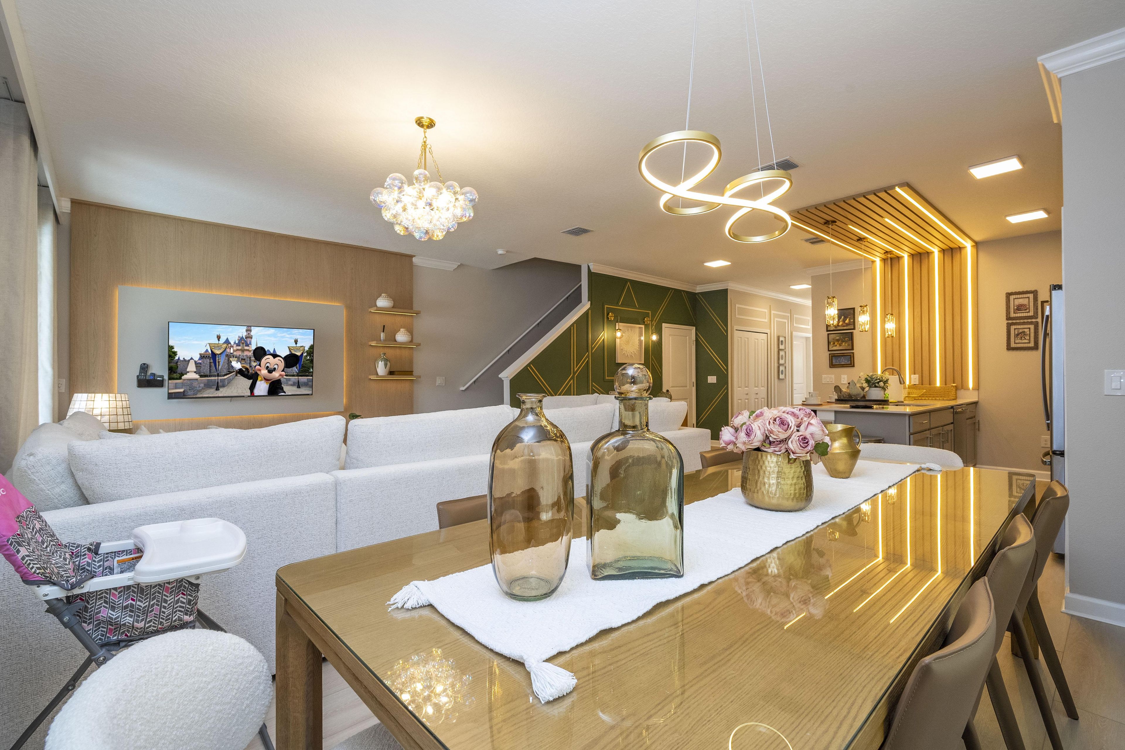 A modern living room with a wooden dining table, white sofa, and a television mounted on the wall.