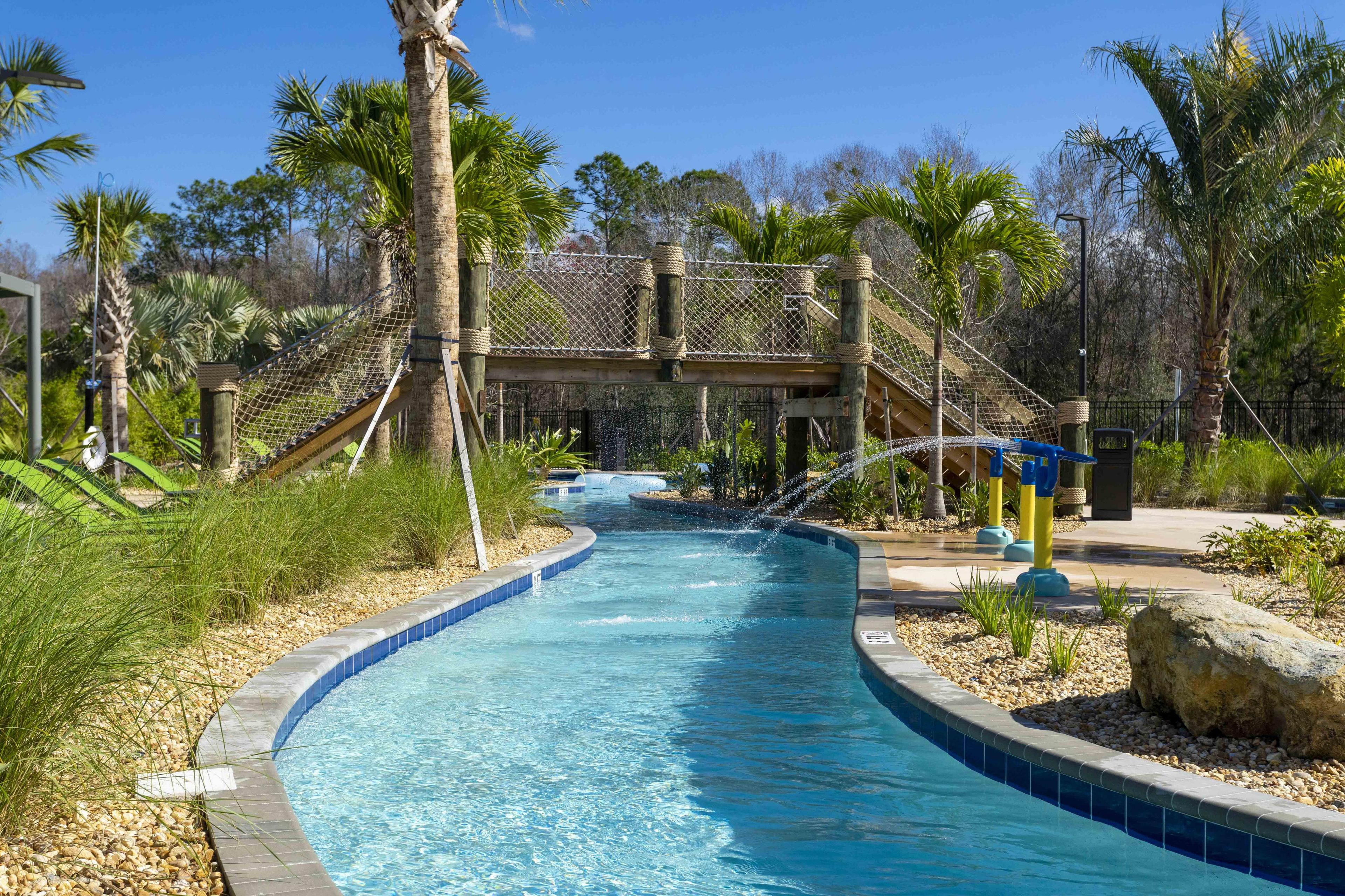 A swimming pool with a curved edge, surrounded by palm trees and a wooden bridge.