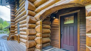 Una cabaña de troncos con una terraza de madera y una puerta de madera oscura.